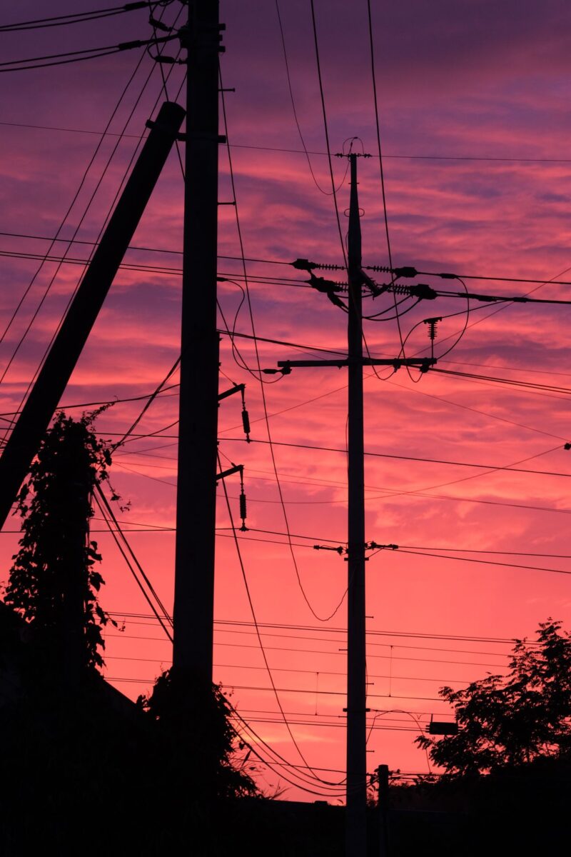 Líneas eléctricas y postes de luz recortados contra un cielo de atardecer, símbolo del cambio de precio de la luz entre el día y la noche